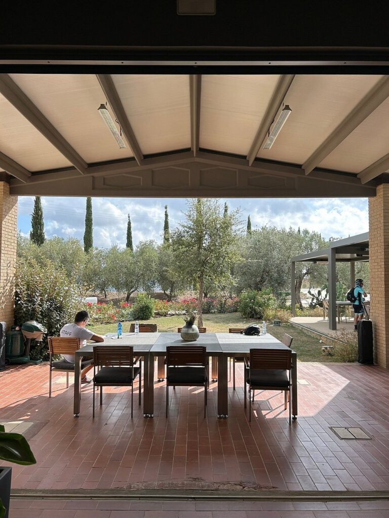 A covered outdoor seating area with a view of olive trees and gardens, perfect for relaxing at a Tuscan villa